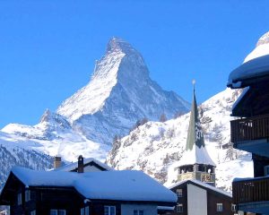 Alps: a village with a tall mountain peak and snow behind it