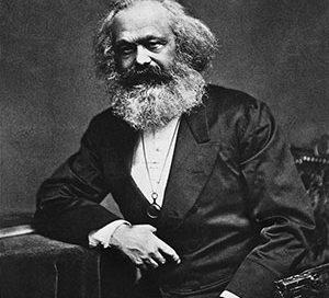 Karl Marx, a white man with long white hair and a very bushy beard, wearing a suit